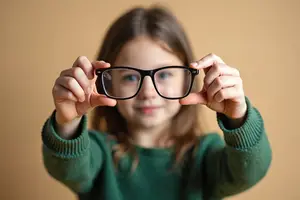 A young girl with glasses holding a pair of glasses