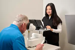 A man wearing a virtual reality headset is getting his eyes examined by a woman in a clinic.