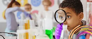 A young boy is using a magnifying glass in a science lab.