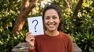 A smiling woman is holding a white piece of paper with a question mark drawn on it in blue marker.