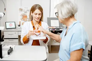 A woman and an elderly woman are examining an eye model in a doctor's office