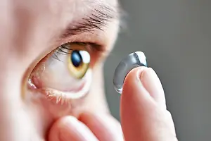 A person is holding a small, shiny, silver contact lens near their eye.