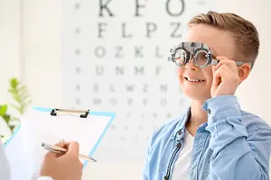 A young boy is having his vision checked by an eye doctor, holding a pair of eyeglasses and looking at the eye chart in front of him.
