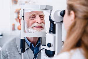 Optometrist examining an elderly man's eyes with a slit lamp