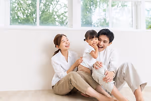 A family of three smiling and sitting on the floor near a window