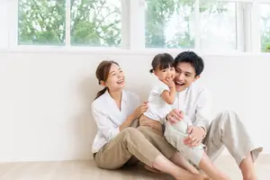 A family of three smiling and sitting on the floor near a window