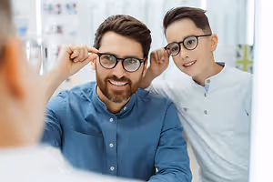 A man and a boy are smiling and looking at their glasses in front of a mirror.