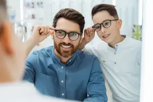 A man and a boy are smiling and looking at their glasses in front of a mirror.