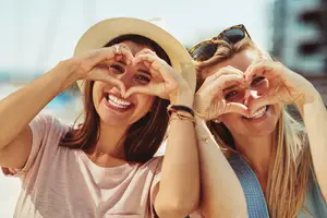 Two young women make a heart shape with their hands, smiling and posing for a picture.