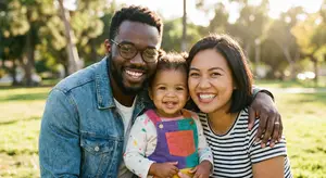 A family is smiling and posing for a photo in a park with trees in the background.