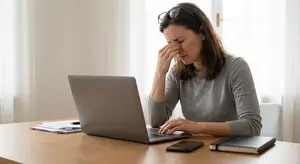 A woman is sitting at a desk with a laptop and looks tired.