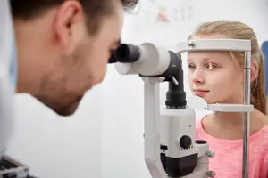 An eye doctor examining a young girl's eye with a slit lamp.