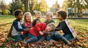 A group of young children play together in a park with leaves on the ground, near a playground.