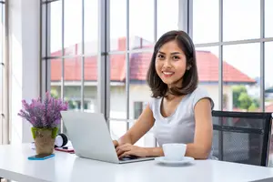 Woman sitting in front of a desk with a laptop and a cup of coffee.