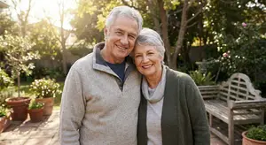 Senior couple standing in their garden on a sunny day, smiling for the camera.
