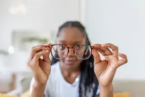 A woman holding glasses in both hands looking down