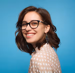 Portrait of a woman with brown hair and glasses smiling in front of a blue background