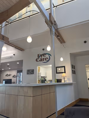 A reception desk in a medical office with a sign that reads Eye Care Professionals, surrounded by lamps and a framed certificate, a monitor on the counter, and a lamp and couch in the background.
