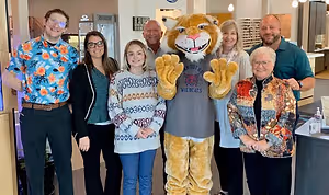People posing for a photo with a mascot, a person in a tiger costume, and a sign on the wall behind them.