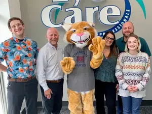Six people posing for a photo in front of a mascot and a sign