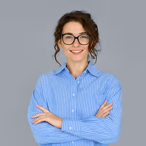A woman in a blue striped shirt and glasses is smiling and posing for a photo with her arms crossed.