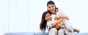 A smiling woman holding a young girl in her arms while sitting on a couch