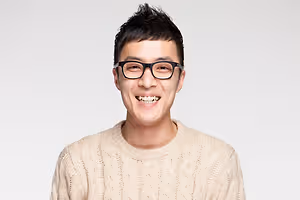 Man wearing glasses and a white sweater smiling for the camera