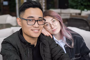 Man with glasses and woman with pink hair sitting on a couch in a restaurant