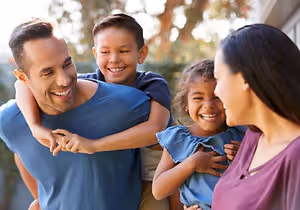 Three people, including a man, a boy, and a girl, are smiling and seem to be posing for a photo in an outdoor area, possibly in a garden.