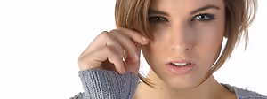A woman with short hair is wearing a gray sweater and has her left hand on her cheek, posing for a photo.