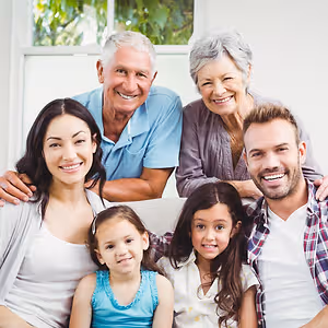Five people in a family are smiling on a couch in front of a window.