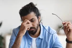 A man with a beard is adjusting his glasses and holding a pair of glasses in his other hand.