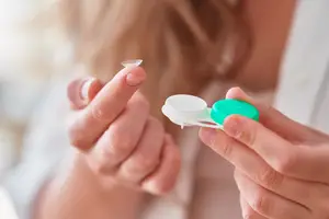 A woman holds a pair of contact lenses in her hand.