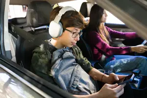 A person in a car wearing headphones is holding a cell phone while the driver is driving the car.