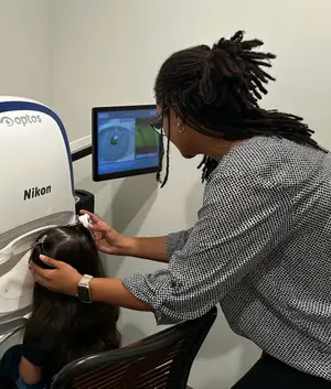 A woman is using a Nikon optos machine on a young girl's eye in a room with white walls