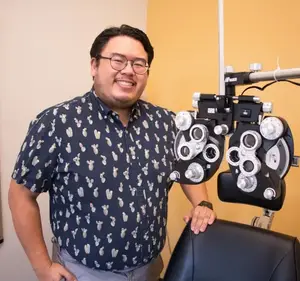 A man standing next to an ophthalmoscope in a room with a yellow wall.