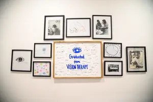 The wall is covered with many frames, one of which is a white board with blue text that reads Graduated from Vision Therapy