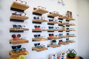 Many wooden shelves with eyeglasses displayed on a white wall