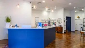 A reception area with a blue counter and a wooden cabinet in a room with white walls and wooden flooring.