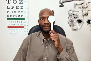 A man is sitting in an eye clinic and holding an eyeglass, probably checking his vision.