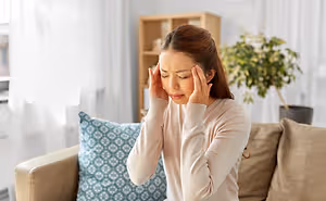 A woman with a headache sitting on a couch in a living room.