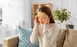 A woman with a headache sitting on a couch in a living room.