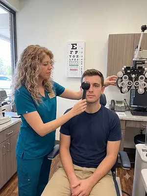 A woman wearing a blue uniform is examining a man's eye using an eye chart and a device.