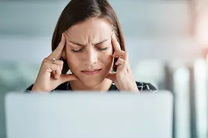 A woman is experiencing a headache while working on her laptop.
