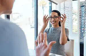 A woman tries on glasses at an optometrist's office and is smiling.