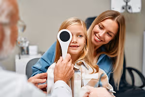 Child having her vision tested with an eye occluder while her mother watches