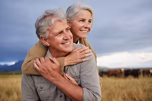 A senior man carrying a woman on his shoulder while smiling in an outdoor area during the daytime