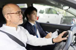 A man in a white shirt is driving a car with a young man sitting in the passenger seat wearing a suit and tie