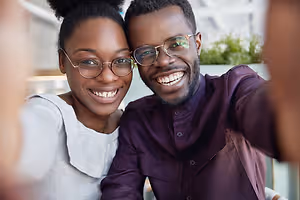 A couple smiling at the camera while wearing glasses