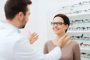 Optometrist speaking with a patient in front of a display of glasses